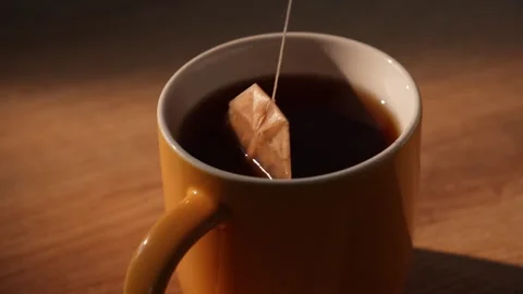 Teabag being pulled from dark brewed tea in yellow mug Video stock 312278534