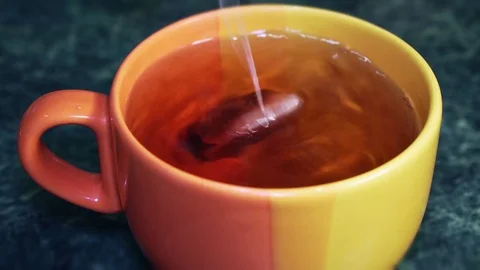 A teabag is dipped in a big orange cup of tea and stirred Stock Footage 103123074