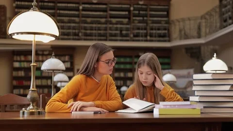 Teacher and children sitting at the table and reading a book in the library.  Stock Footage 159626892