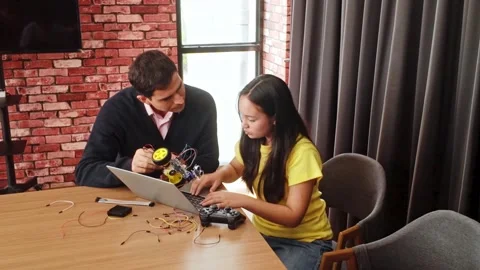 A teacher and student collaborate on coding a wheeled robot in a STEM class. Stock Footage 313877935
