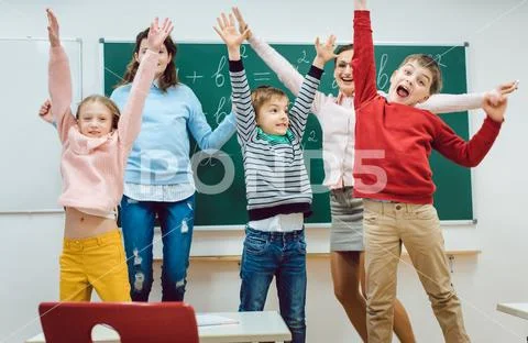 Teacher and students of primary school jumping in classroom Stock Photos