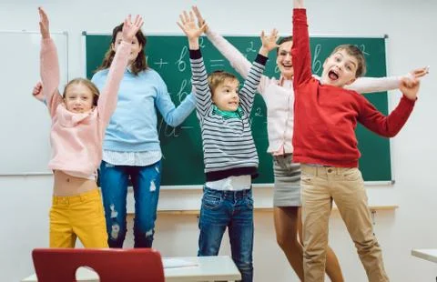 Teacher and students of primary school jumping in classroom Stock Photos