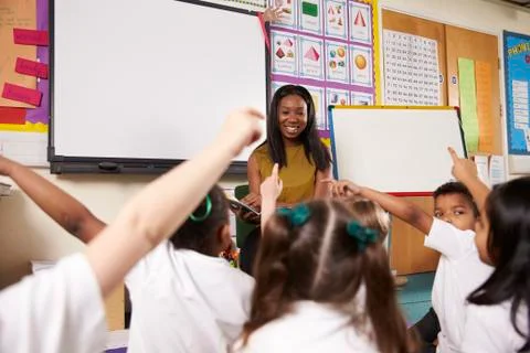 Teacher Asks Elementary School Pupils Question In Classroom Stock Photos