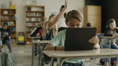 Teacher assisting girl raising hand in classroom reading digital tablet ,Provo, Stock Footage