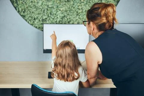 Teacher assisting schoolgirl while computer class at primary school. Child .. Stock Photos