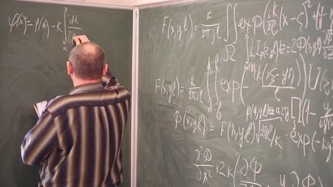 Teacher copying integral equations from book to blackboard in classroom. Stock Footage 69988232
