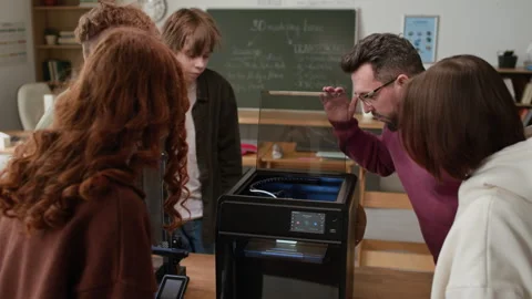 Teacher Demonstrating Inner Workings of 3D Printer to Group of Focused Students Stockbeeldmateriaal 335697241