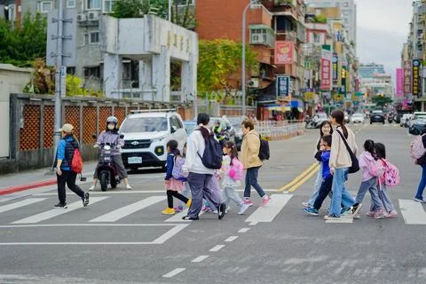 Teacher escorting students across pedestrian crosswalk as motorcyclist waits 库存照片