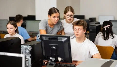 Teacher explaining task solution to young girl and boys during computer science Stock Photos