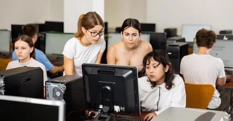Teacher explaining task solution to young girl and boys during computer science Fotos Stock