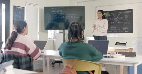 Teacher gesturing to scrolling code on screen as teaching students in class with Stock Footage 341028982