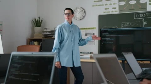 Teacher Gesturing Towards Code Displayed on Monitor, her Students Listening Video stock 317638066