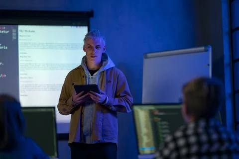 Teacher giving computer science lecture to young students in dark room. Room Foto stock
