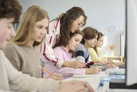 Teacher guiding teens on computers in modern classroom for collaborative Stock Photos