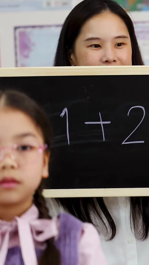 Teacher Helping Elementary Student Solve Math Equation on Chalkboard Vidéo 329215912