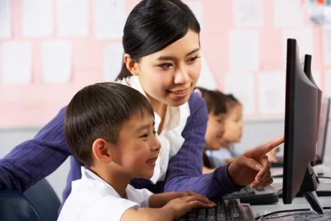 Teacher helping student during computer class in chinese school classroom Stock Photos
