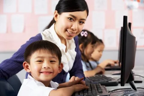 Teacher helping student during computer class in chinese school classroom Stock Photos