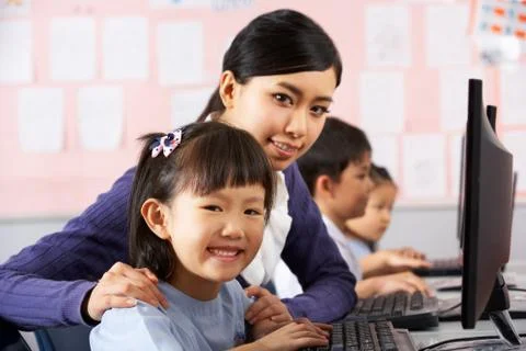 Teacher helping student during computer class in chinese school classroom Stock Photos