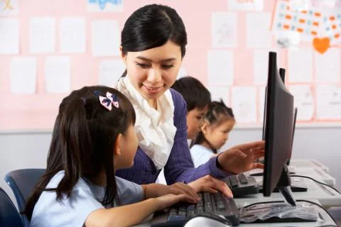 Teacher helping student during computer class in chinese school classroom Stock Photos
