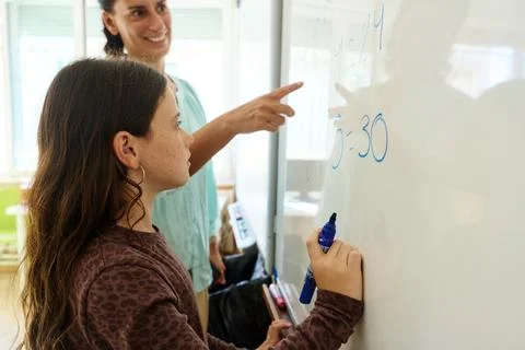 Teacher helping student solving math problem on whiteboard Foto stock