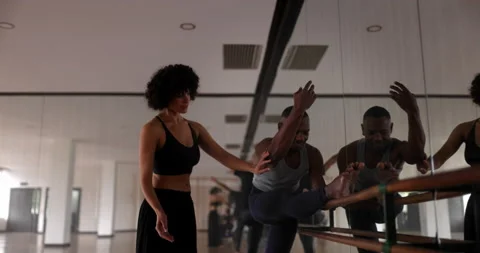 Teacher helping student stretch leg on barre in dance studio Stock Footage 147356104