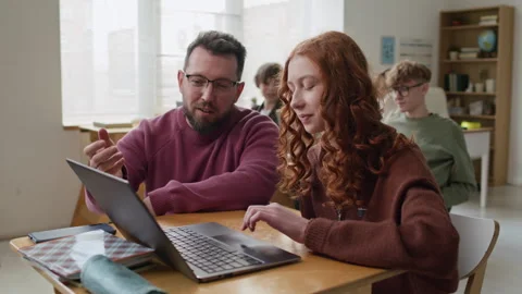 Teacher Helping Student with Task on her Laptop at Desk in School Stock Footage 335694409