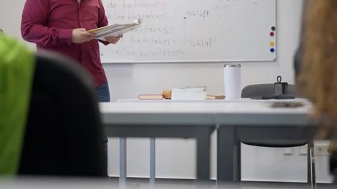 A teacher is immersed in a book while in a classroom with a whiteboard and a Stock Footage 303597758