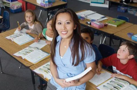 Teacher Leaning On Desk While Students Looking At Her Stock Photos