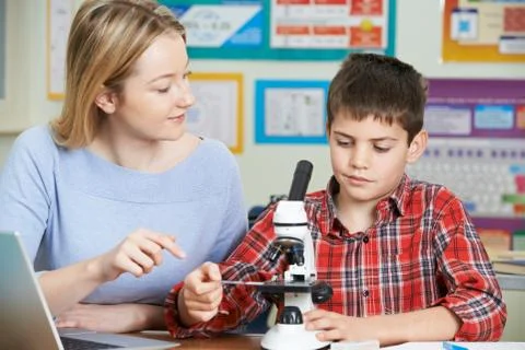 Teacher With Male Student Using Microscope In Science Class Stock Photos