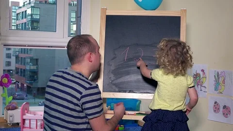 Teacher man writing numbers on chalk black board for little child girl Stock Footage