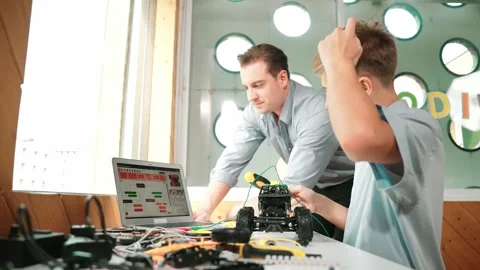 Teacher pointing at laptop screen while student fixing car model. Edification Stock Footage 278759217