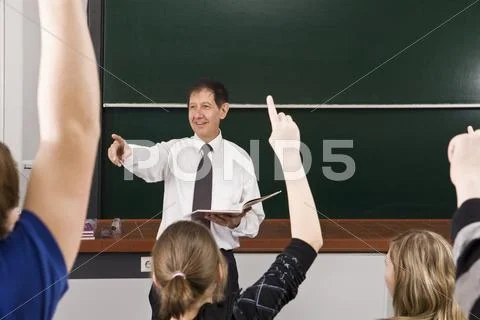 A teacher points while his students raise their hands in a classroom Stock Photos