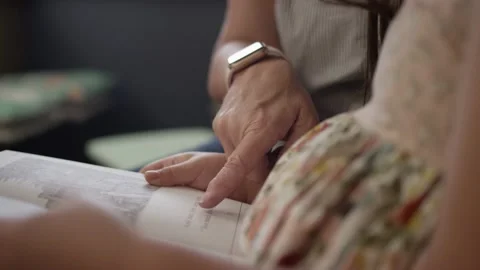 Teacher points at words in book and helps young girl read book in classroom Video stock 168652906