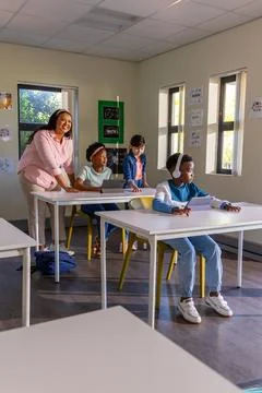Teacher with school-age class helping boy wearing over-ear headphones using Foto stock