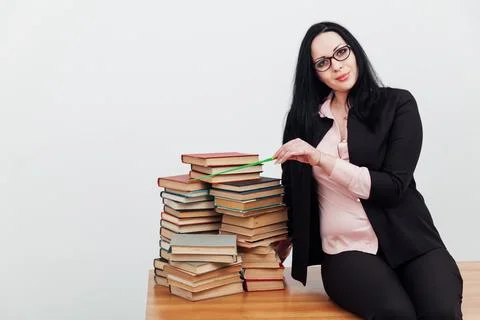 A teacher with a school pointer sits on a table with many books Stock Photos