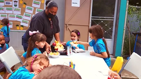 Teacher Serving Food Outside Classroom to Group of Elementary Students Stock Footage 221925361