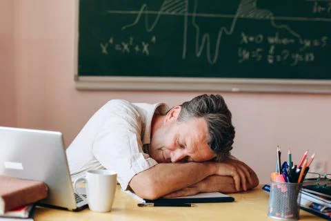 Teacher sleeping in the classroom, head down on the his hands Stock Photos