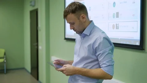 Teacher standing alone in front of class of students and touching his pad while Видео 70934160