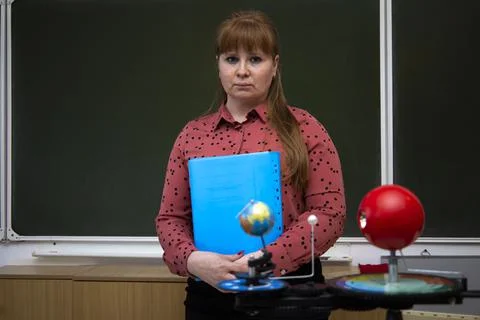 The teacher stands near the blackboard with a folder in his hands. Stock Photos
