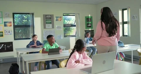 Teacher teaching teens in pink top walking, bending in classroom urging laptop Stock Footage 344948504