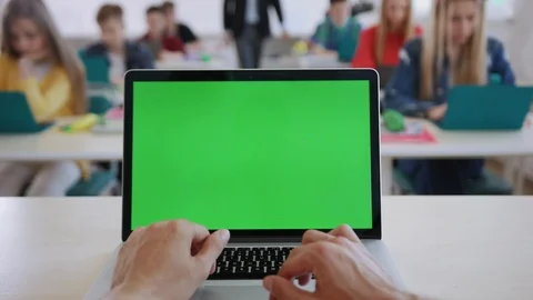 Teacher using a computer laptop with greenscreen mockup sitting in front of the Stock Footage 111549537