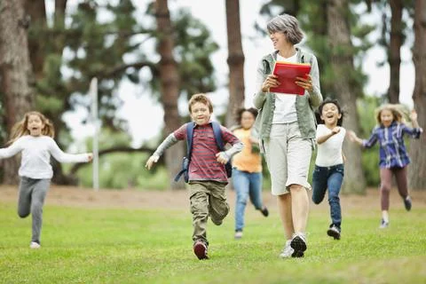 Teacher walking at park while students run in background 스톡 사진