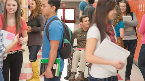 A teacher in a wheelchair talks a groups of students standing in the hallway Video stock 33891618
