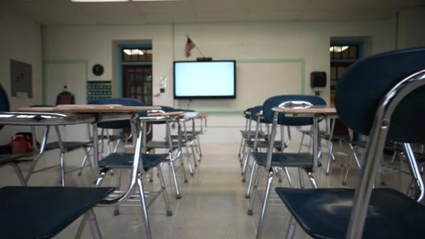 Teacher working in background while camera moves across the backs of empty Stock Footage 246773429