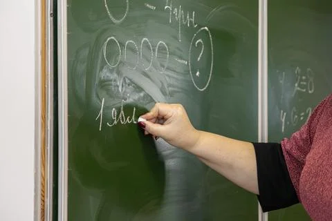A teacher writes complex math exercises with white chalk on a green classro.. Stock Photos