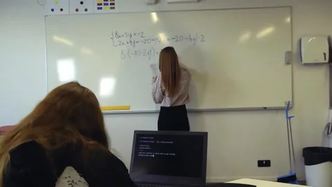 Teacher writing a math equation on a whiteboard for a student Stockbeeldmateriaal 345479049