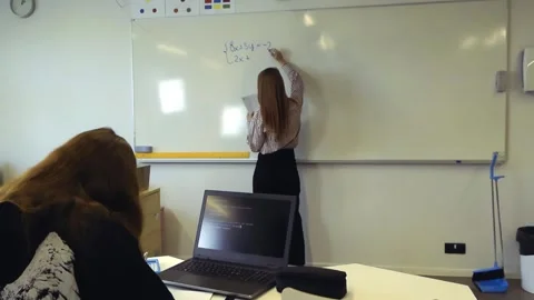 Teacher writing a math equation on the whiteboard for a student Stockbeeldmateriaal 345480083