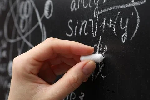 Teacher writing math formulas with chalk on blackboard, closeup Stock Photos