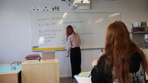 Teacher writing mathematics problems on whiteboard while student learning Stock-Fotos
