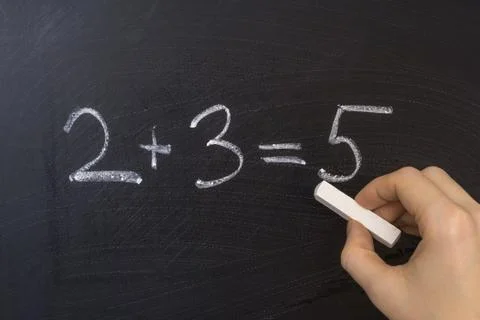 Teacher is writing simple math equation on blackboard with chalk Stock Photos